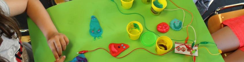 Hands of children, working on a green desk table with colorful plasticine (first steps in easy making with makey makey) 