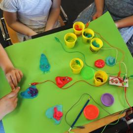Hands of children, working on a green desk table with colorful plasticine (first steps in easy making with makey makey) 